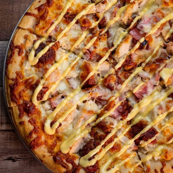 Close-up of a This Guy's Pizza with chicken, bacon, cheese, and a mustard drizzle.