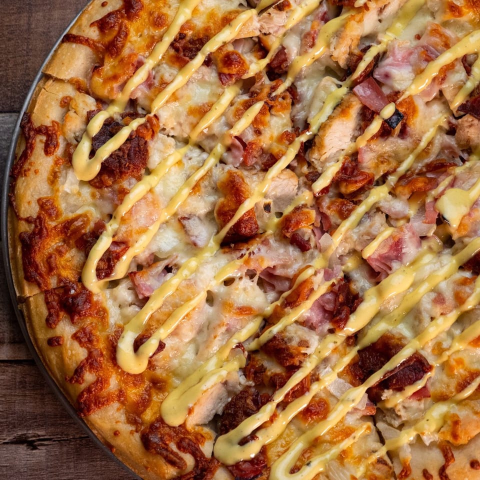Close-up of a This Guy's Pizza chicken and bacon pizza with a mustard drizzle.