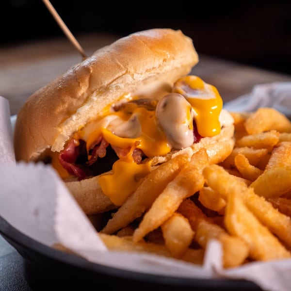 Cheesy hot dog with bacon and mushrooms, served with a side of golden french fries.
