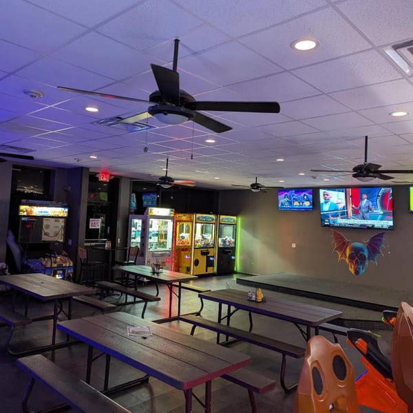 The 78 Pub's interior with picnic tables, arcade games, TVs, and a stage with a skull decoration.