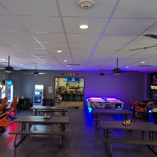 The 78 Pub's game room with picnic tables, arcade games, and a view into the bar area.