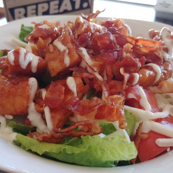 A close-up of a salad with crispy bacon, fried chicken, lettuce, tomatoes, and ranch dressing.